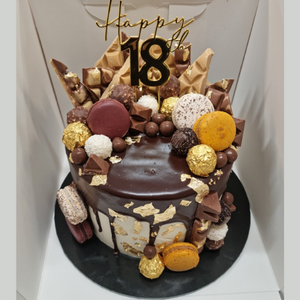 chocolate drip cake with gold leaf and topped with various chocolates and macaroons