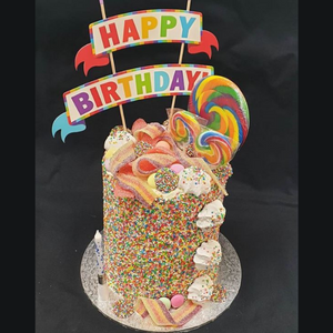 birthday cake covered in sprinkles, lollies, rainbow lollipops and a happy birthday topper