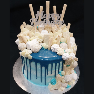 blue custom mudcake with blue drip and topped with assorted white chocolates and meringues