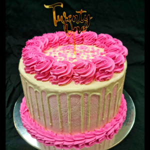 Stacked mudcake with pink icing, white drip and topped with pink icing rosettes and a gold twenty one cake topper