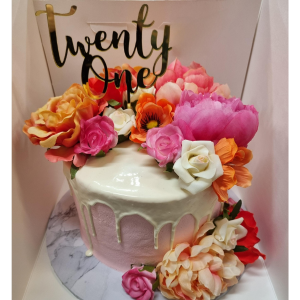 Stacked mudcake with pink ganache, white chocolate drip and topped with assorted artificial flowers and a 21 cake topper