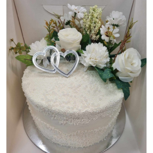 double stacked mudcake encased in white pearl sprinkles, topped with artificial flowers and silver hearts